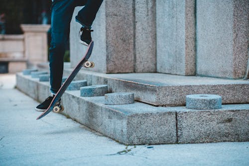 Unrecognizable male skater jumping on skateboard while doing trick on street near concrete block in street in city during training