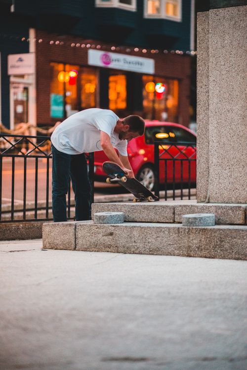 Free Side view of anonymous young male leaning forward with skateboard near urban road in evening Stock Photo