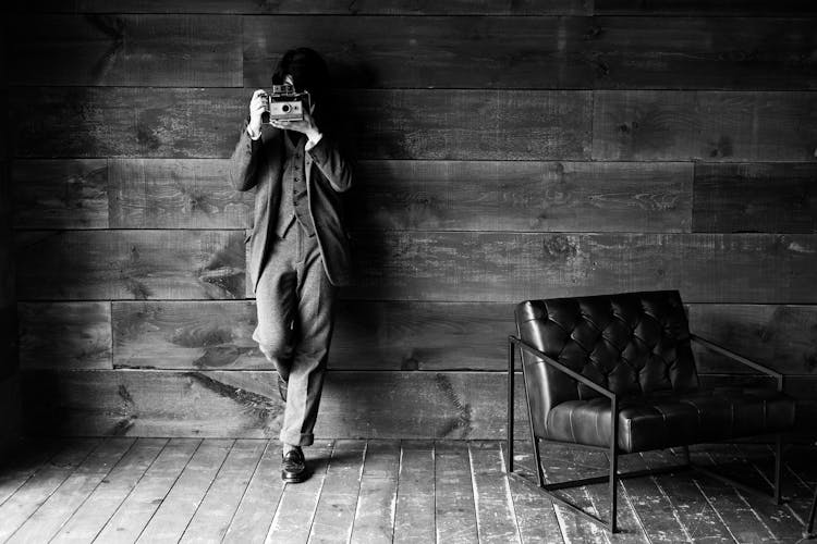 Grayscale Photo Of A Person Leaning On A Wooden Wall Taking Picture