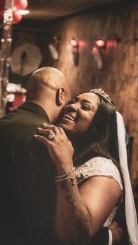 Anonymous African American bald groom in elegant suit and ethnic laughing female embracing together on blurred background
