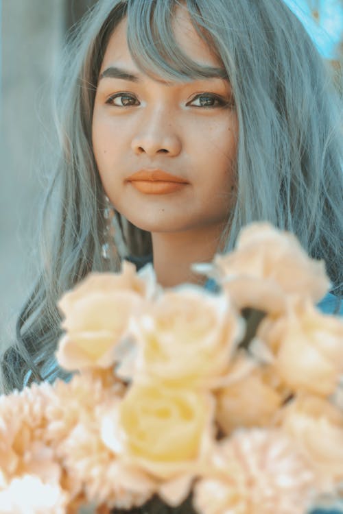 Free Serious young Asian female in makeup with bouquet of flowers looking at camera in sunny day Stock Photo