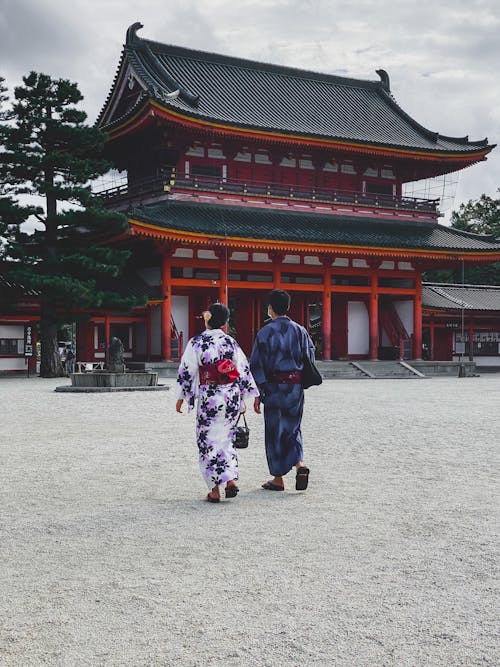 People Wearing Traditional Kimonos Walking Near a Red and Black Temple