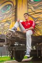 Man in Red and White Long Sleeve Shirt and Gray Pants Sitting on Brown Metal Train