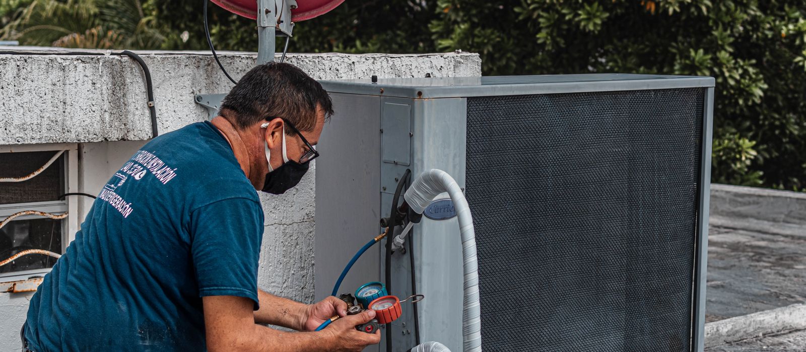 Technician servicing an outdoor air conditioner with a manifold gauge