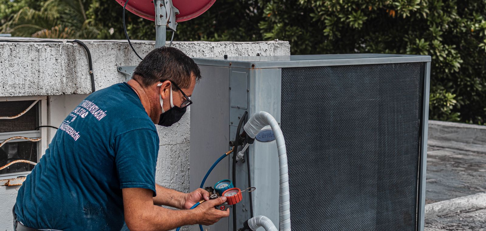 Technician servicing an outdoor air conditioner with a manifold gauge
