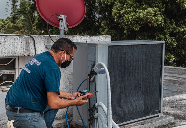 Technician servicing an outdoor air conditioner with a manifold gauge
