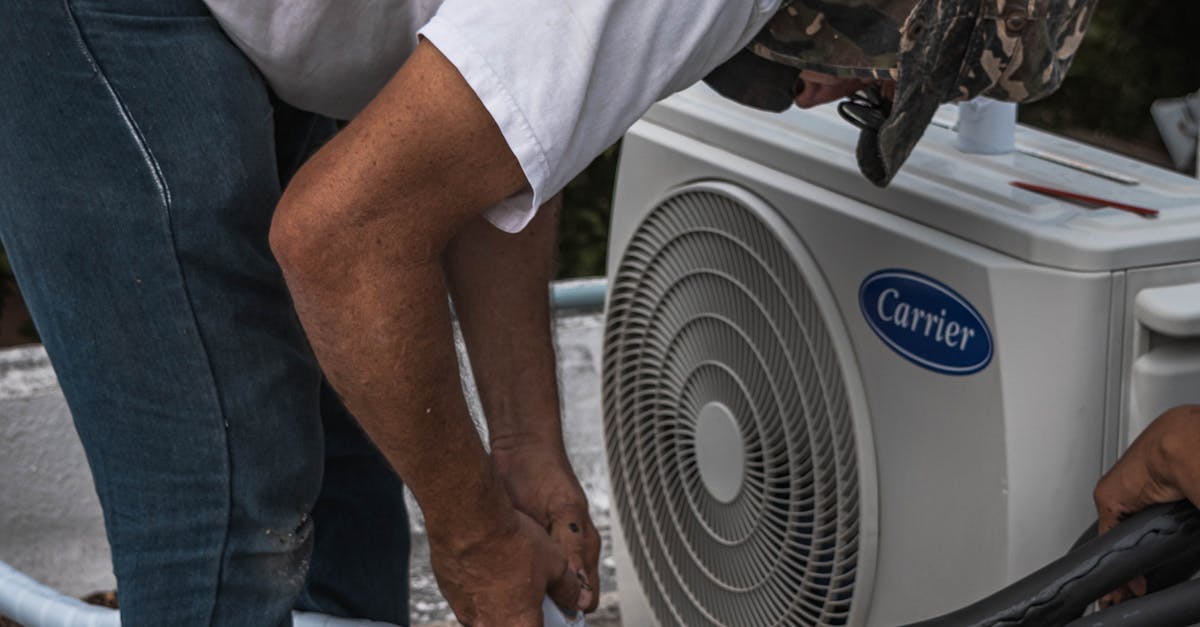 A technician performs maintenance on an outdoor air conditioning unit, focusing on hose connections.