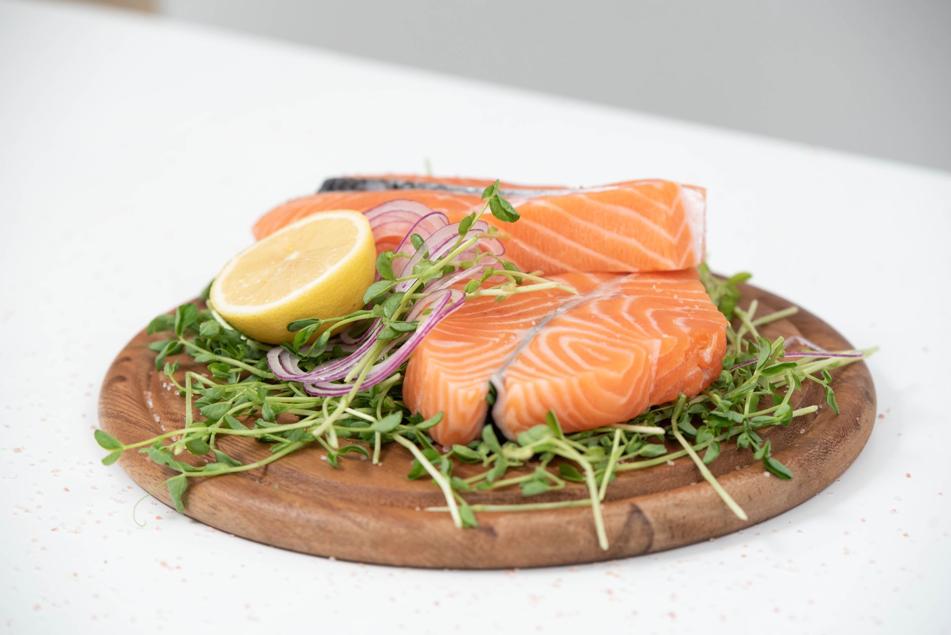 Close-up of fresh salmon slices with lemon and microgreens on a wooden platter. Ideal for food-related themes.