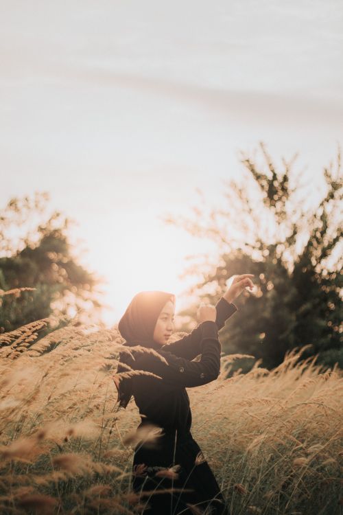 Free A woman in a hijab stands gracefully in a sunlit field of tall grass, capturing tranquility and beauty. Stock Photo