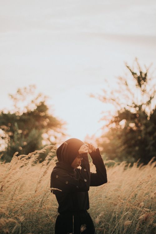 Free A serene moment of a woman in hijab adjusting her headscarf amidst tall grass, captured at sunset. Stock Photo