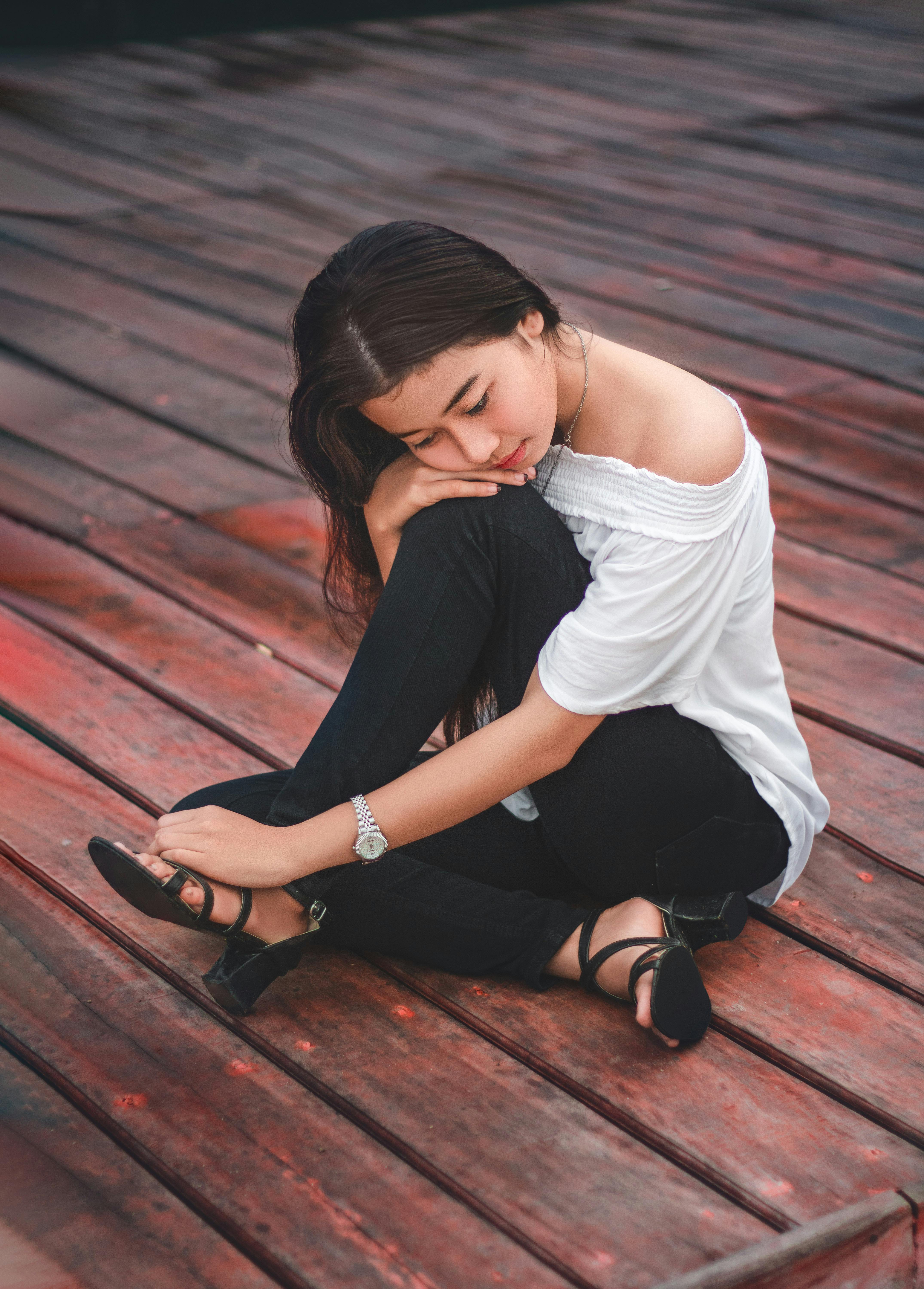 Woman in White Tank Top and Black Pants Sitting on Brown Wooden Floor