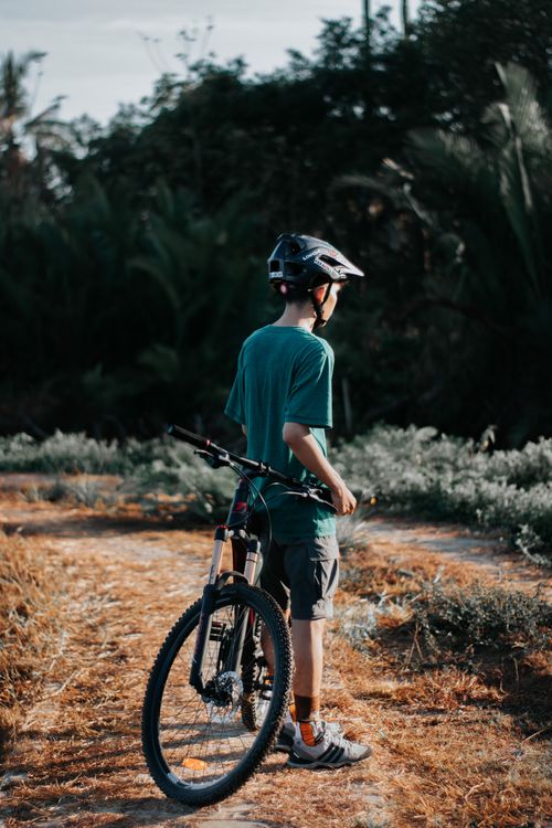 Free Back view of anonymous male biker in protective helmet standing near modern bicycle on walkway and looking away Stock Photo