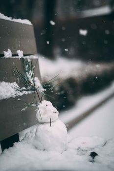冬日大雪中，公园的长凳上坐着一个迷人的小雪人，四周雪花纷飞