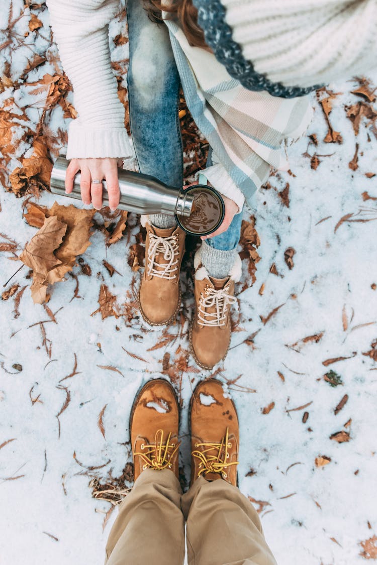 Couple Sitting On Snow While Having Coffee