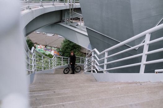 一名身穿黑色夹克的男子抱着自行车，站在城市里涂鸦背景的混凝土楼梯上