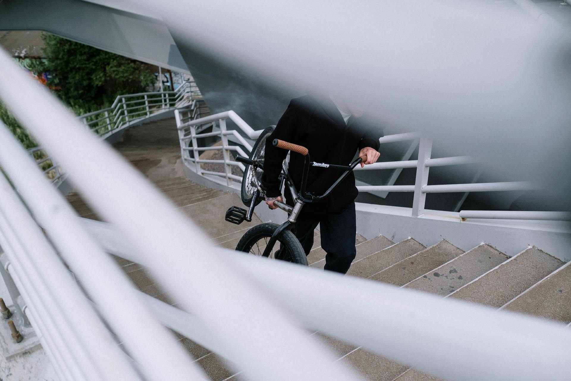 Person in Black Jacket Carrying a Bicycle While Going Upstairs