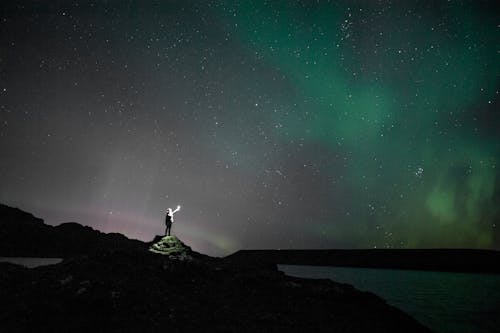 Silhouette of Person Standing on Rock Under Starry Night