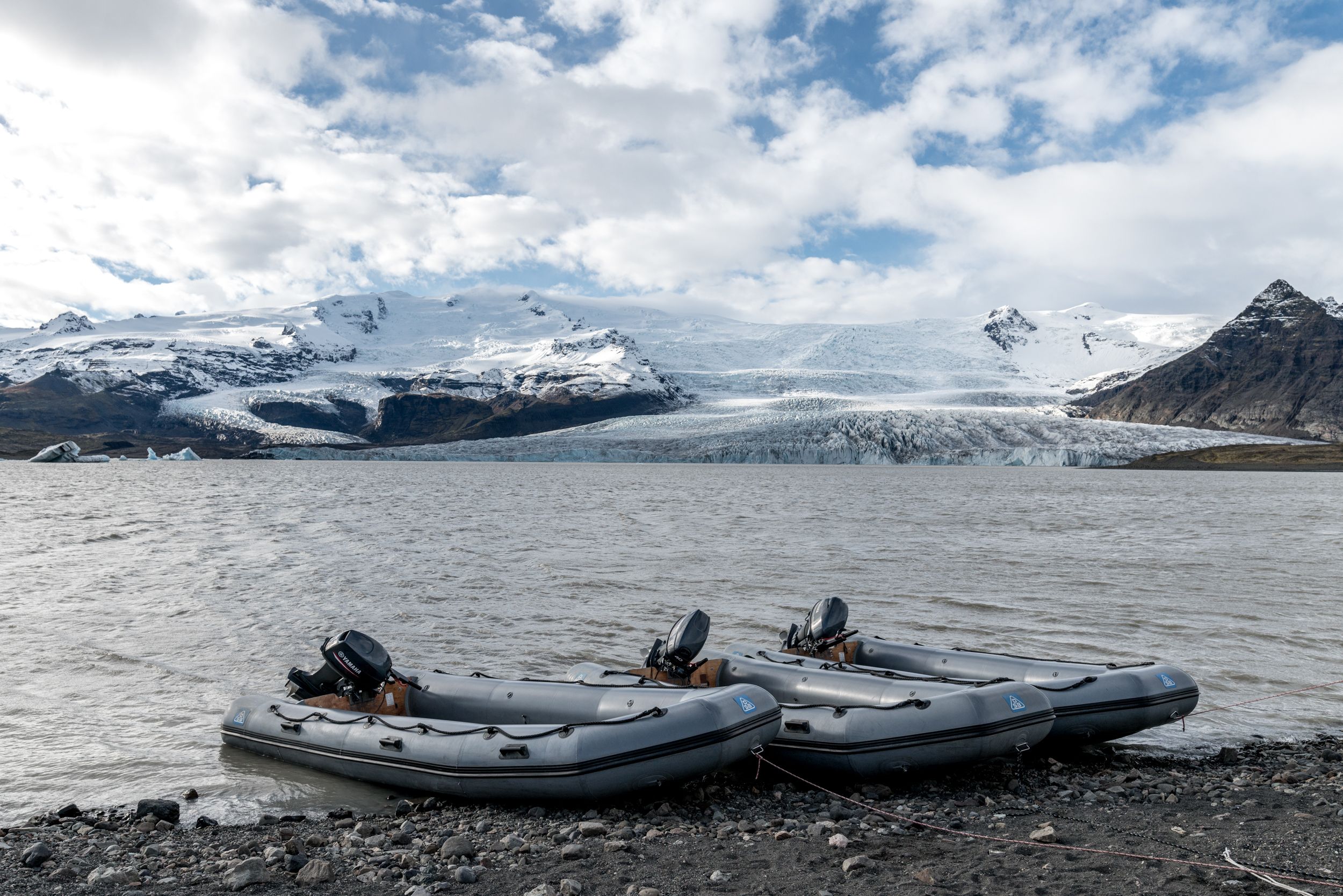 Inflatable boats on a glacial lake shore with snow-covered mountains in Iceland.