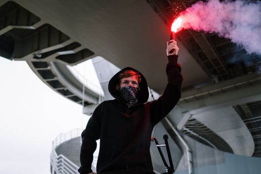 一名身穿连帽衫的年轻人在一座现代桥下举起耀斑，营造出戏剧性的场景