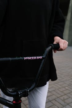 A bmx cyclist holding the handlebars of a bike outdoors, focusing on the 'Princess BMX' design.