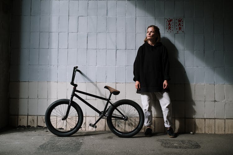 Man Wearing A Black Hoodie Standing Beside A Black Bike