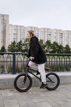 Woman riding a BMX bike in an urban setting by a river on a cloudy day.