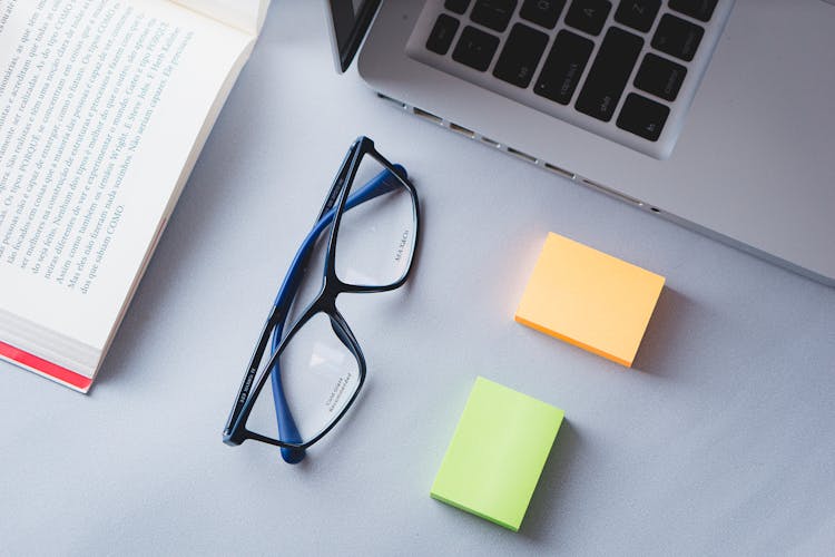 Eyeglasses, Sticky Notes And A Book Lying On A Desk Next To A Laptop 