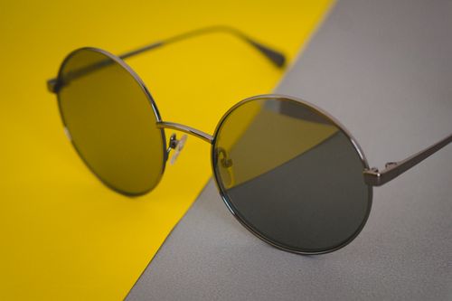Free Close-up of round sunglasses on a vibrant yellow and grey background. Perfect for fashion and accessory concepts. Stock Photo