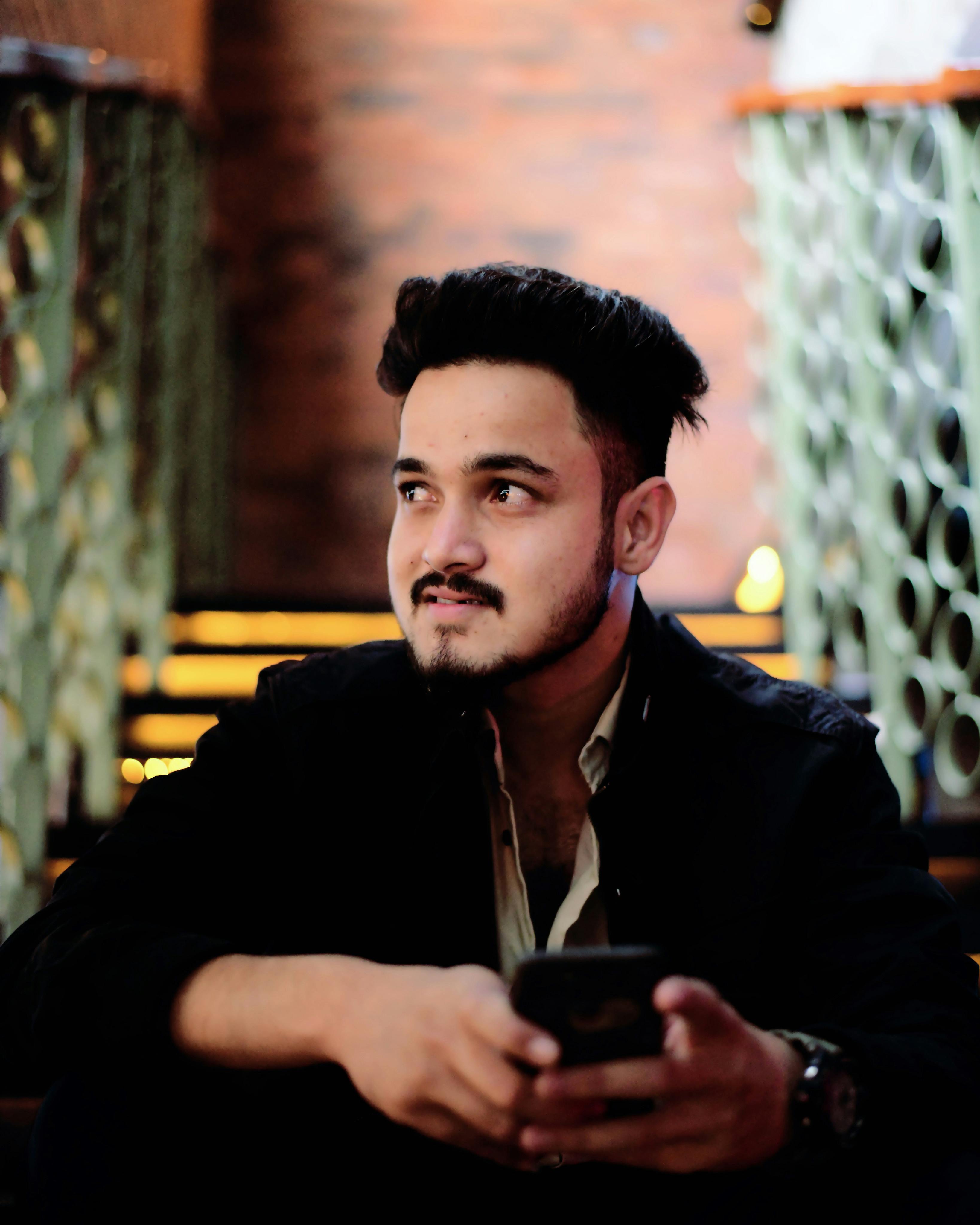 Portrait of a young man with a smartphone in a stylish Bengaluru cafe, exhibiting modern lifestyle.