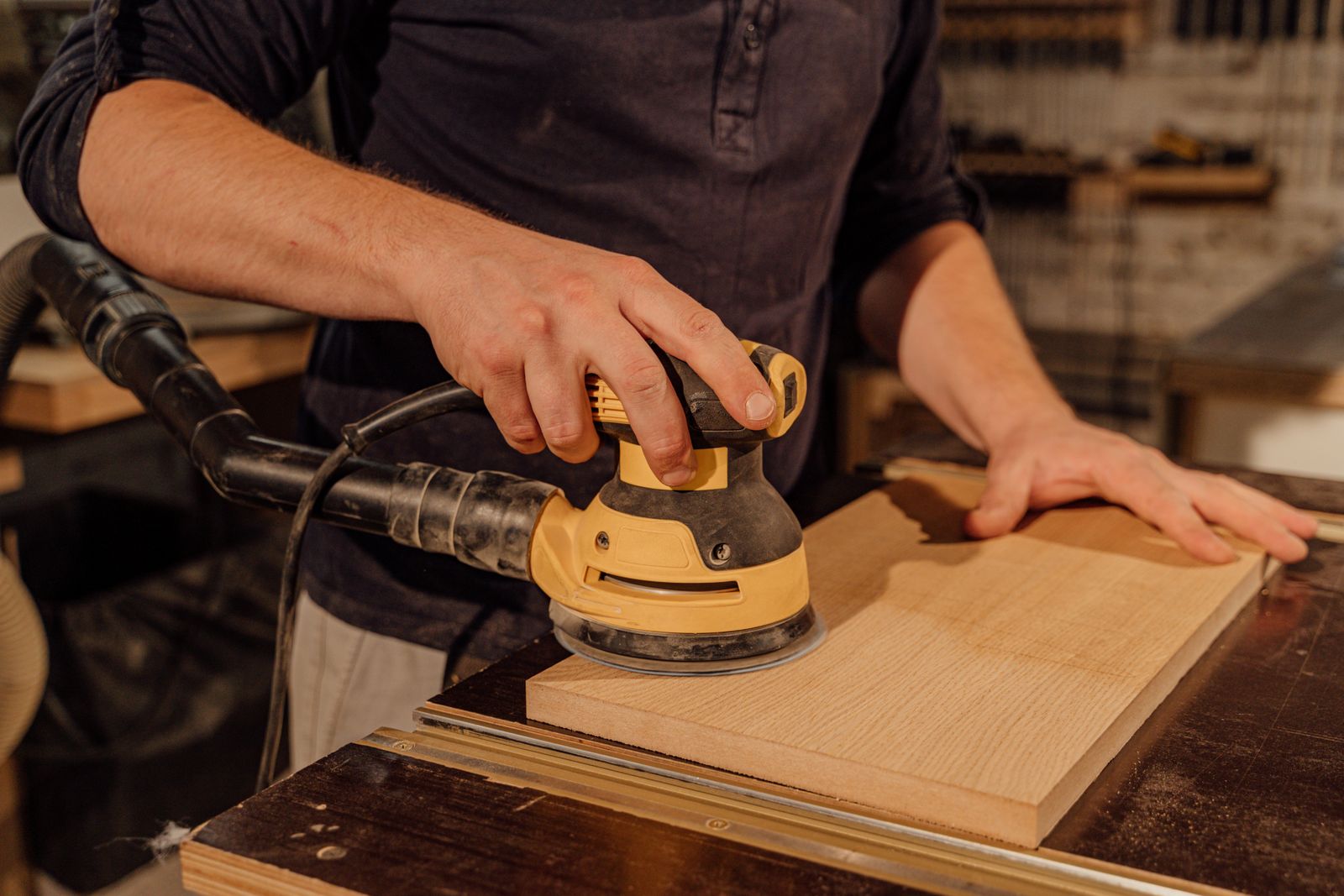 Carpenter sanding a wooden board in a workshop, evoking the hours of hand-sanding that separate handcrafted from machine-made