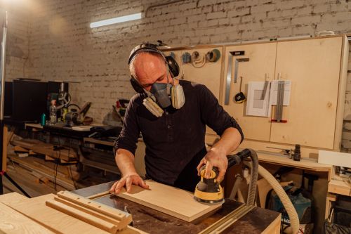 Free Craftsman wearing safety gear while sanding wood indoors. Focus on precision and safety in woodworking. Stock Photo