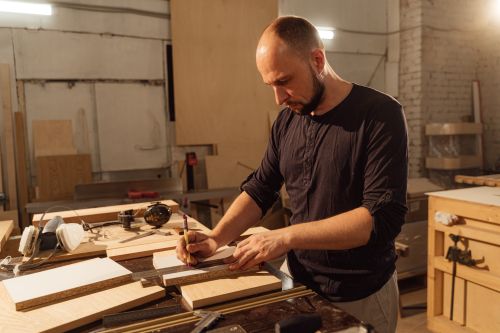 Free A focused craftsman measures wood planks in a workshop, emphasizing precision woodworking skills. Stock Photo