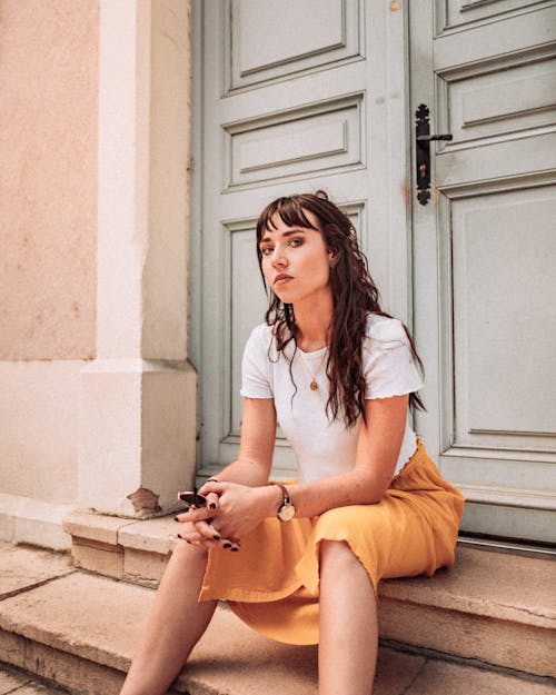 Woman in White Shirt and Yellow Skirt Sitting on Brown Concrete Stairs