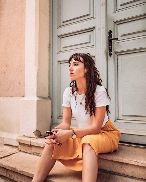 Woman in White Crew Neck T-shirt and Yellow Skirt Sitting on Brown Concrete Stairs