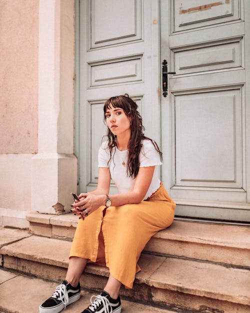 Woman in White Tank Top and Orange Skirt Sitting on Brown Concrete Stairs