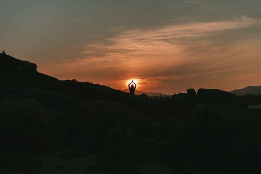 A serene yoga silhouette against a sunset backdrop amidst rocky landscape.