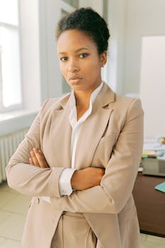 African American businesswoman confidently standing with arms crossed in a modern office setting.