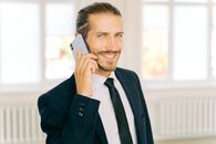 一位穿着西装、打着领带的自信商人，在室内微笑着打电话