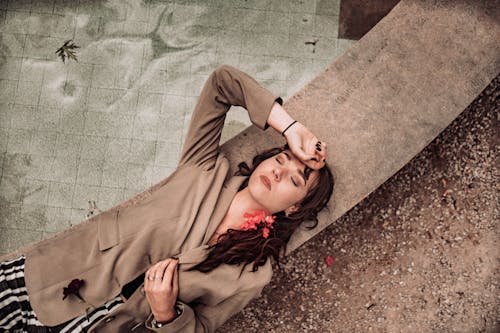 Woman in Brown Long Sleeve Dress Lying on Concrete Floor