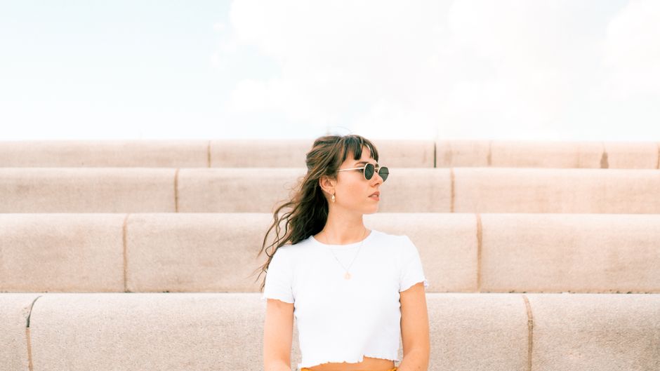 Fashionable young woman with sunglasses sits on stone steps, exuding a modern and relaxed vibe.