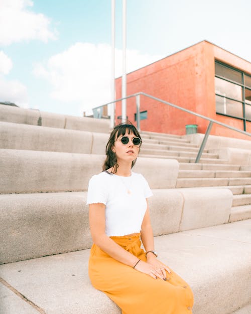 Woman in White Shirt and Yellow Skirt Sitting on Concrete Stairs