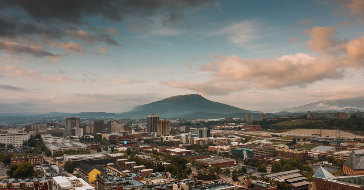 Spectacular scenery of contemporary city district located near mountains against cloudy sunset sky