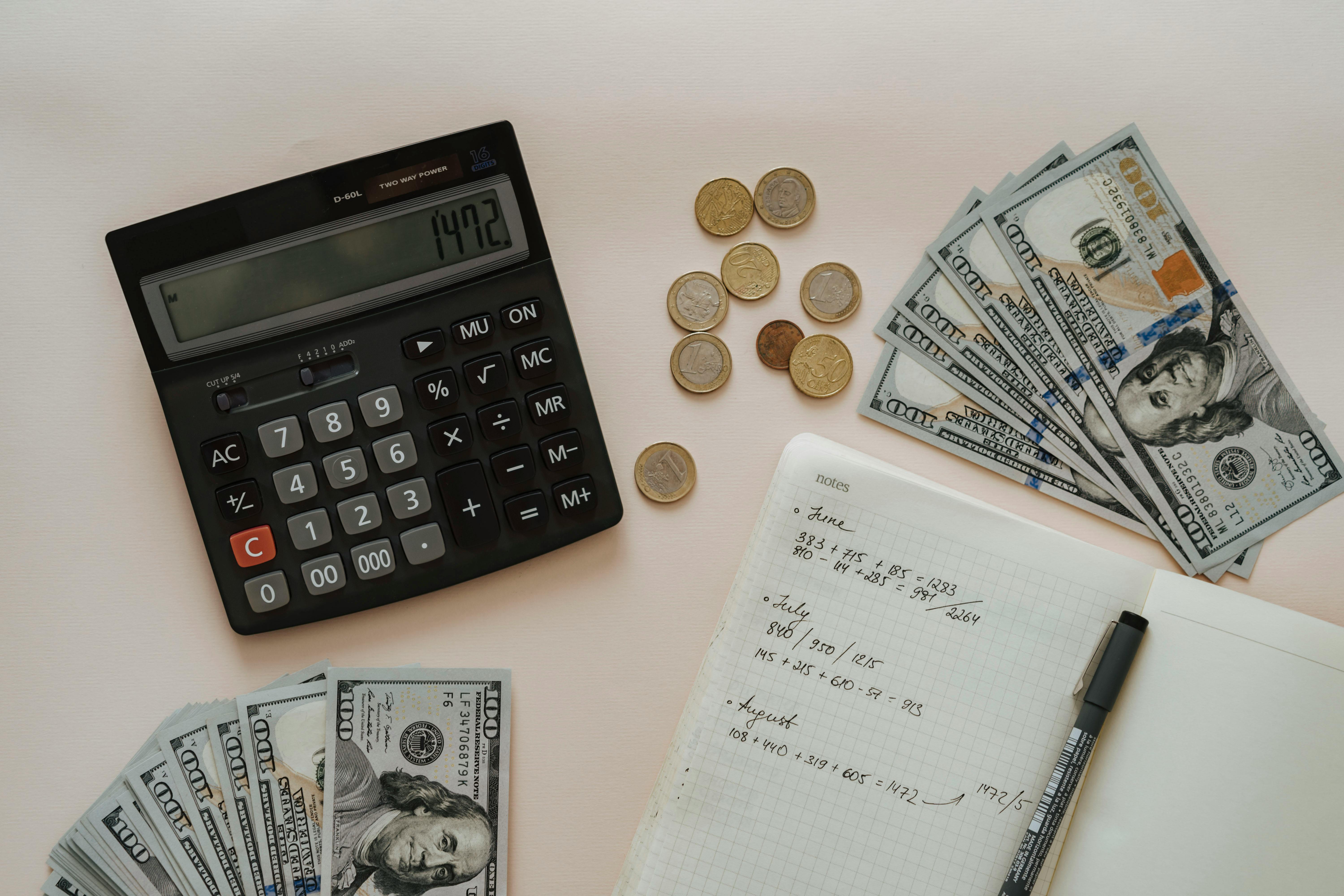 black calculator beside coins and notebook