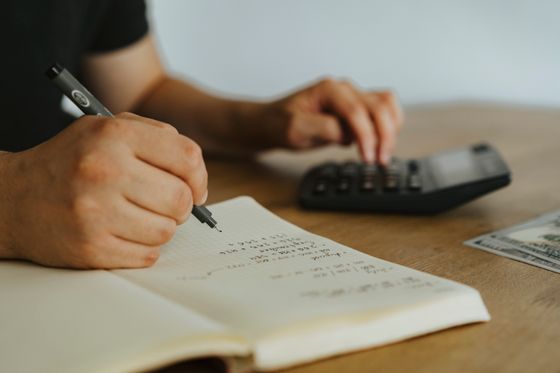 Hands writing calculations beside a calculator — photo by olia danilevich on Pexels