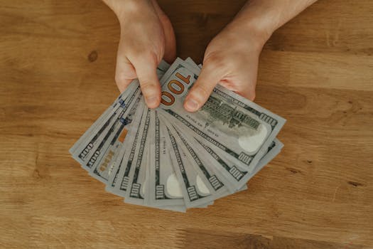 Close-up of hands fanning out US hundred dollar bills on a wooden table.