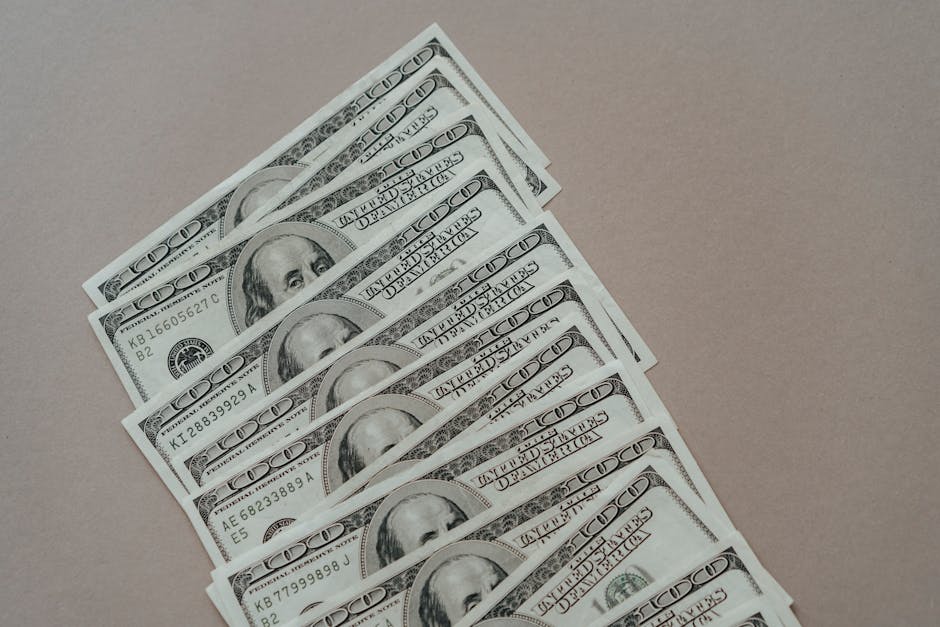 A close-up of multiple US dollar bills arranged on a neutral surface.