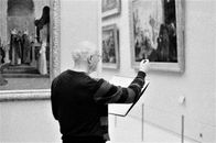 Black and White Photo with Grain of a Man Sketching in an art Gallery