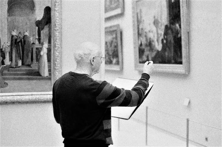 Black And White Photo With Grain Of A Man Sketching In An Art Gallery