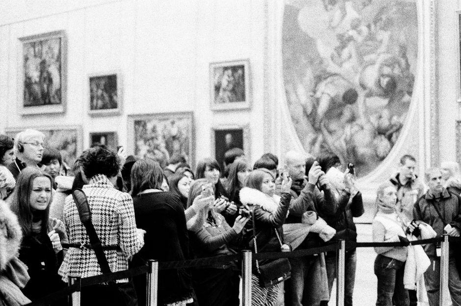 Black and white image of a crowd photographing art in a gallery setting.