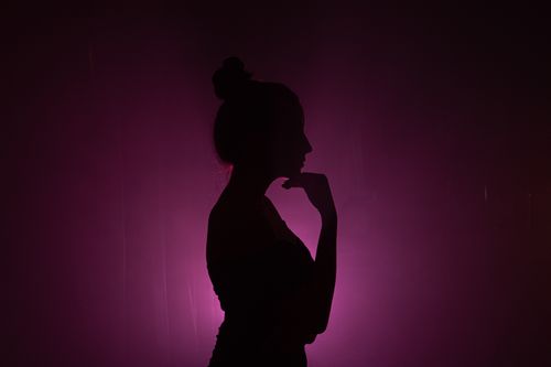 Free Artistic silhouette of a woman with hand on chin against a vibrant purple light background. Stock Photo
